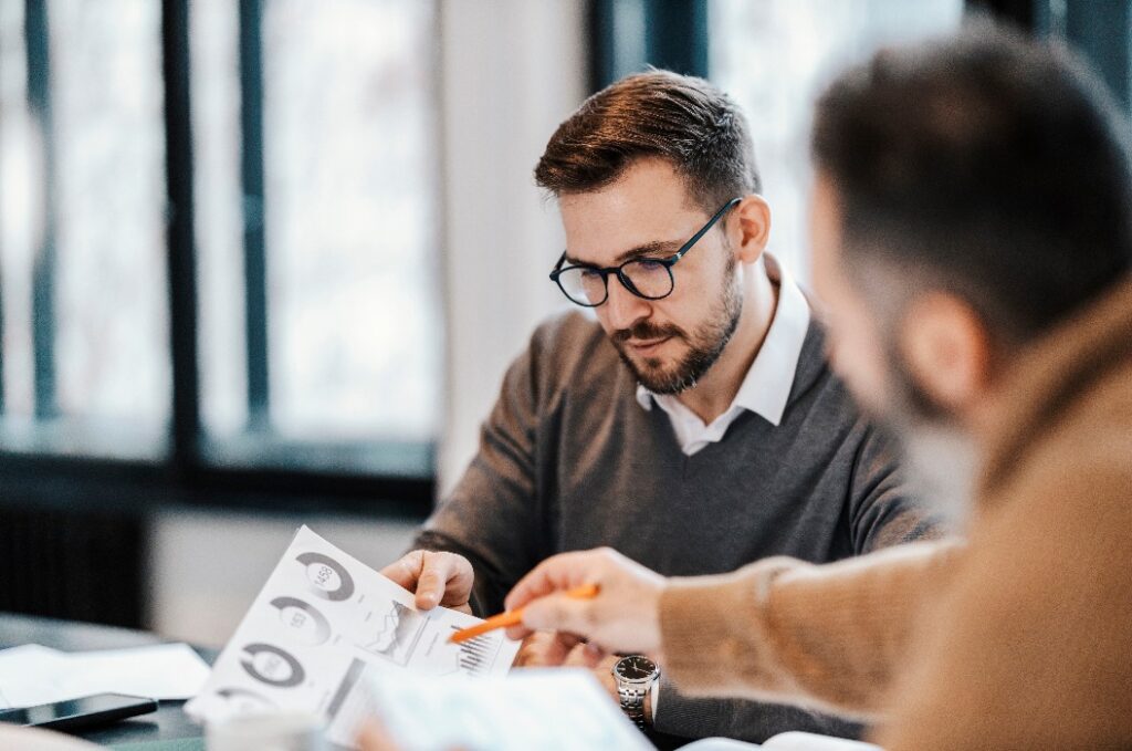 Zwei Kollegen sitzen im Besprechungsraum und diskutieren über Diagramme und Statistiken.